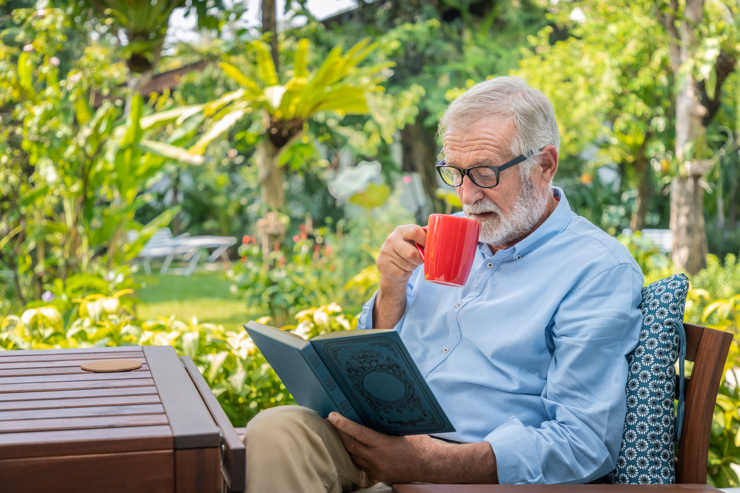 Willa Seniora w Buczkowicach - senior elderly man reading book drinking mug coffee garden scaled